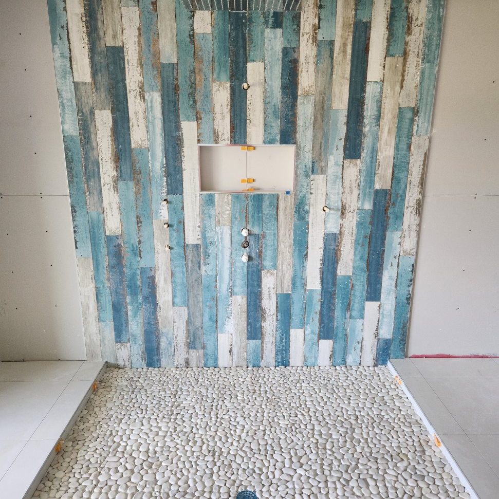 Blue glass tile shower with pebble shower pan