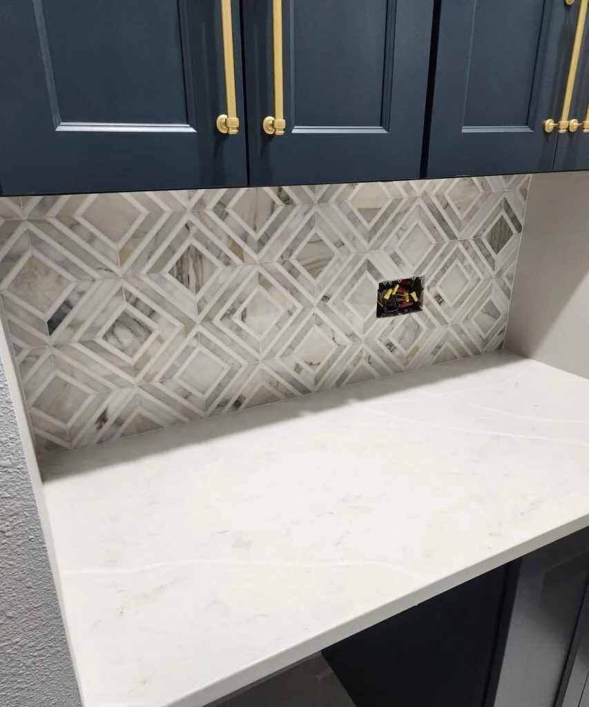 Geometric mosaic tile backsplash with navy cabinets